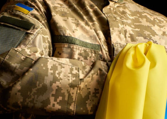 Ukrainian soldier holds in his hand the yellow-blue flag of the state, he pressed his hand to his chest, concept of the memory of the dead soldiers, close up